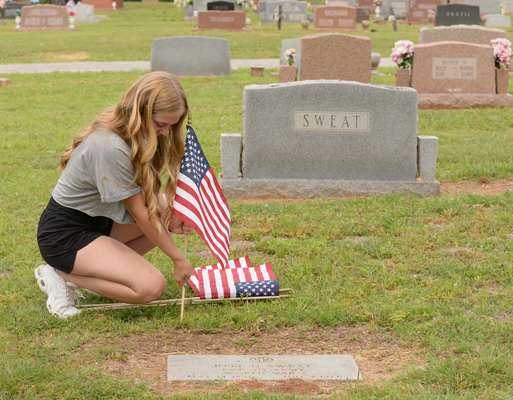 Macy Heaton, 17, of Marlow, pushes a small American flag into place near the gravestone of Roy D. Sweat, a private in the U.S. Army during World War I, on Saturday, May 27, 2023. Heaton was one of a small group of students from Marlow, Bray-Doyle and Central High who volunteered to help place new American flags at the gravestones of military service members, in honor of Memorial Day weekend. Photo by Toni Hopper/The Marlow Review